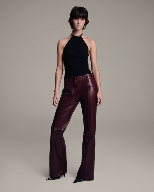 Model wearing a black halter top with burgundy leather flared trousers, full-length front view against a taupe background