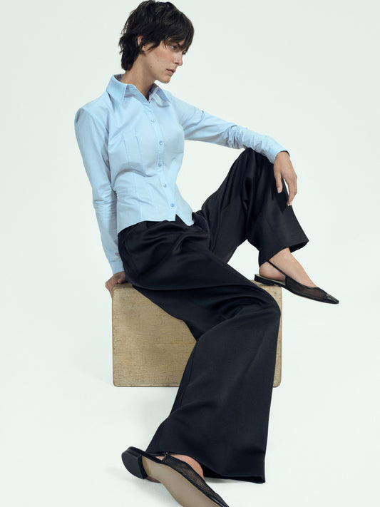 Person wearing a light blue shirt and black pants sitting on a wooden block against a white background