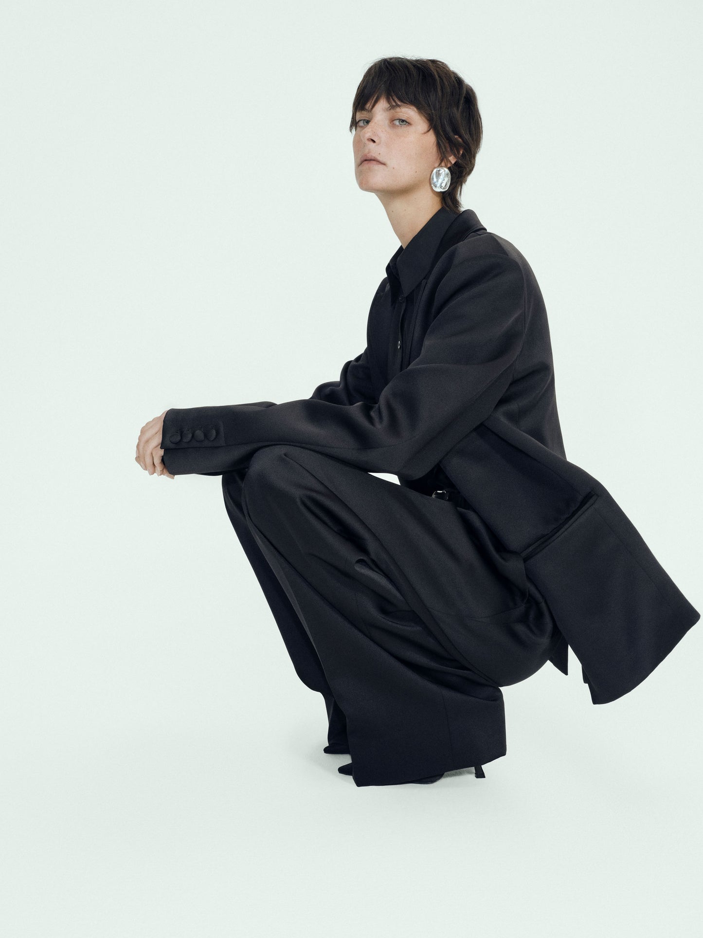 Person wearing a black satin coat sitting on a white background
