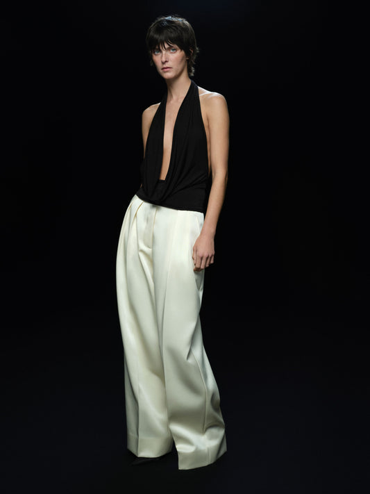 Woman wearing a black halter top and custard satin wide-leg pants on a black background