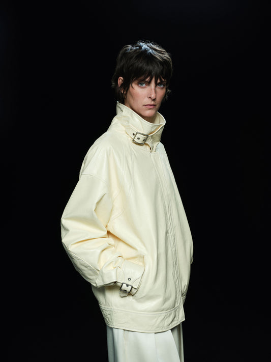 Person wearing a cream lambskin leather jacket against a black background