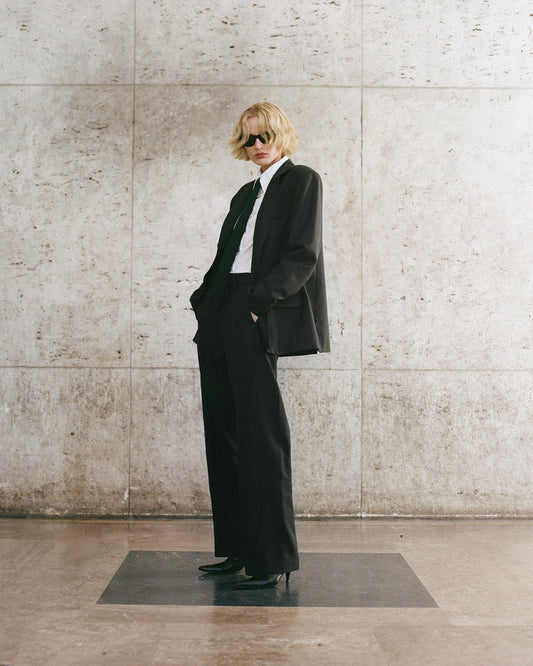 Person wearing a chic green suit standing against a stone wall.