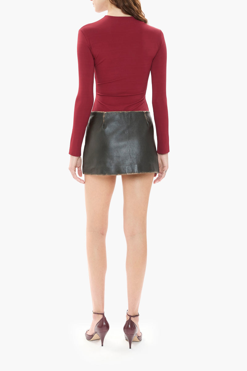 Person wearing a burgundy red long-sleeve top and black leather skirt on a white background