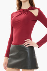 Woman wearing a burgundy red long-sleeve top with cut-out design and black leather skirt on a white background