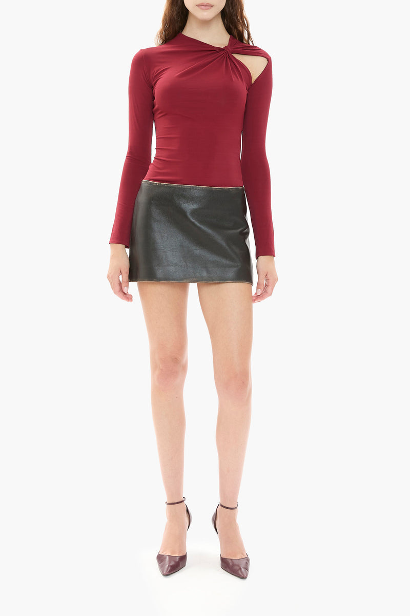 Person wearing a burgundy red long-sleeve top and black leather skirt on a white background