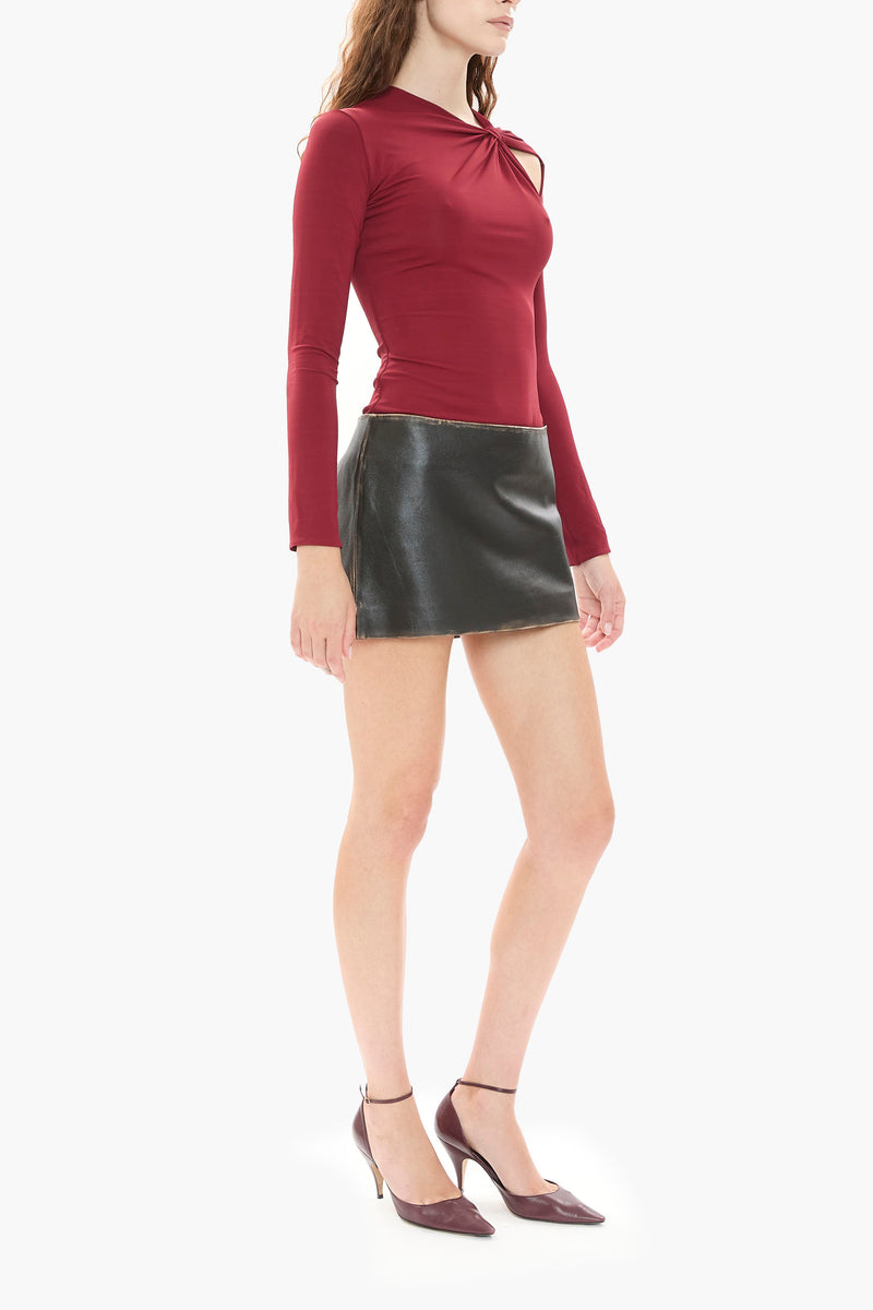 Woman wearing a burgundy red long-sleeve top and black leather mini skirt on a white background