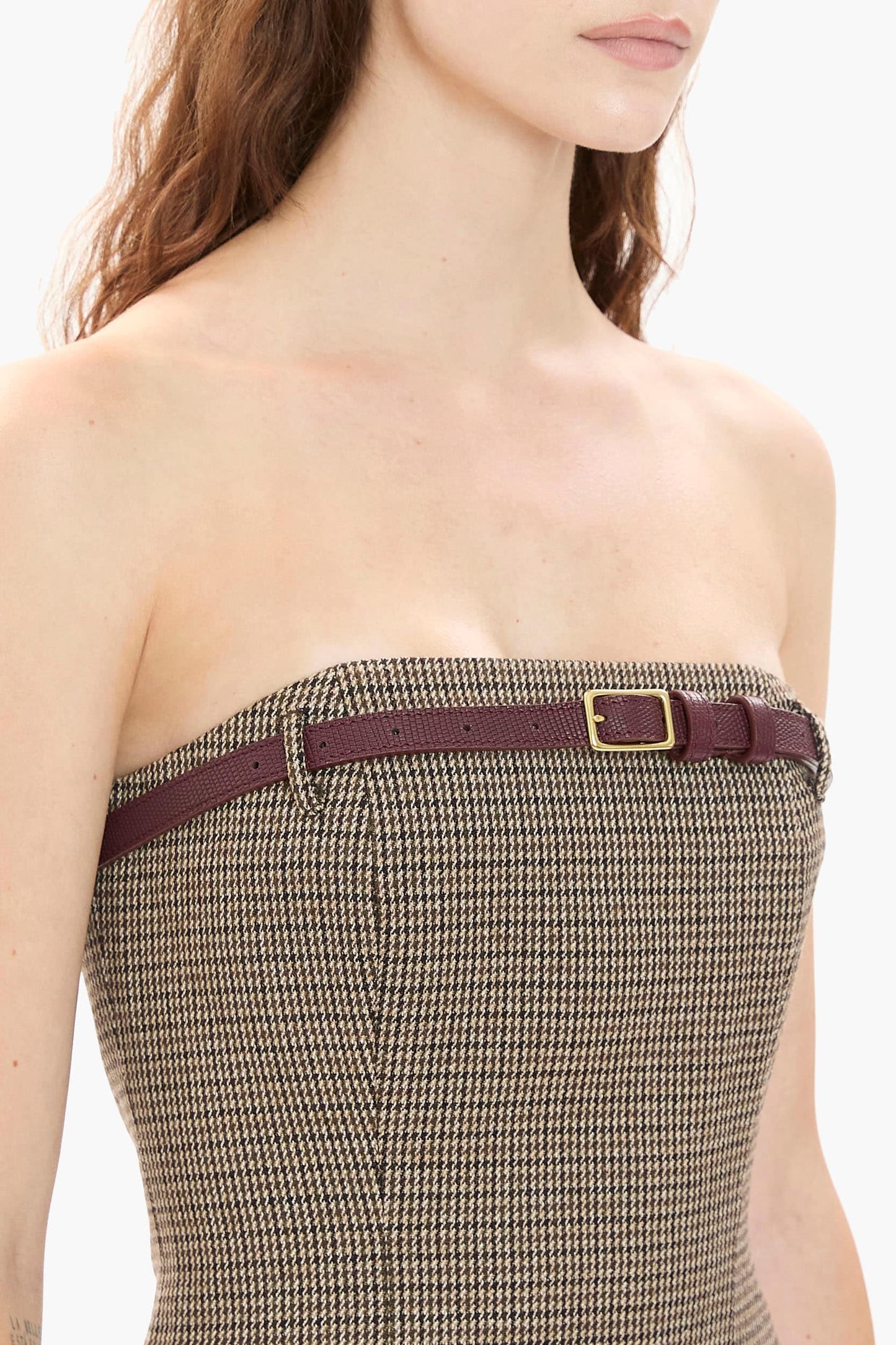 Close up of a strapless brown houndstooth mini dress with a belt worn by a model on a white background