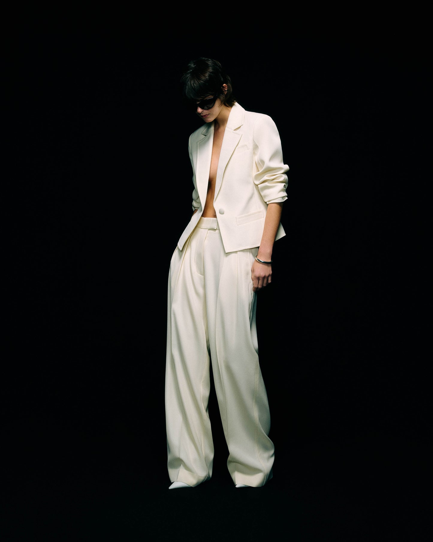 Model wearing a cream blazer worn open over wide-leg cream trousers, full-length front view against a black background