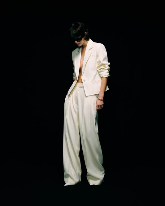 Model wearing a cream blazer worn open over wide-leg cream trousers, full-length front view against a black background