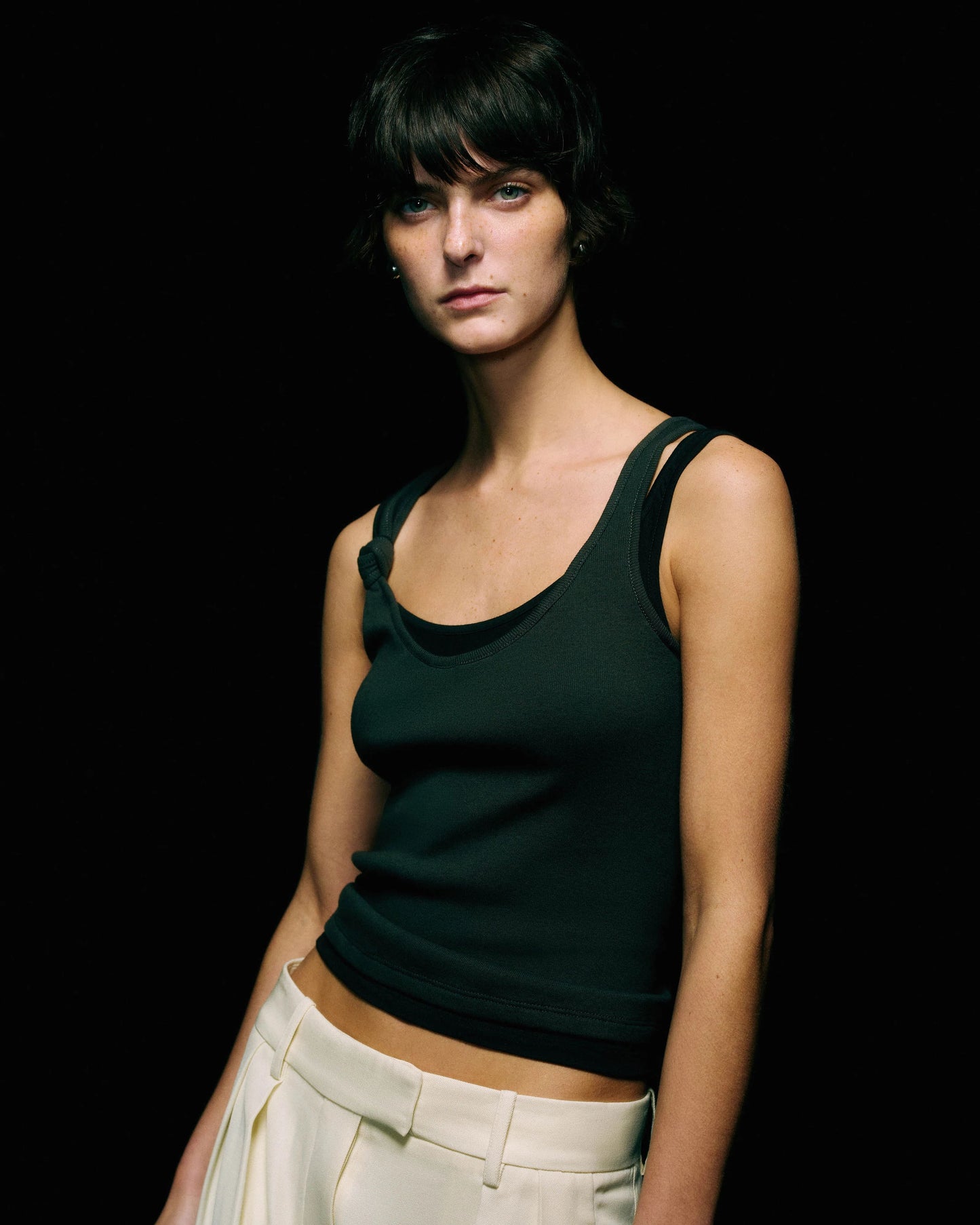 Model in a black ribbed tank top with a layered double-strap neckline, waist-up view against a black background