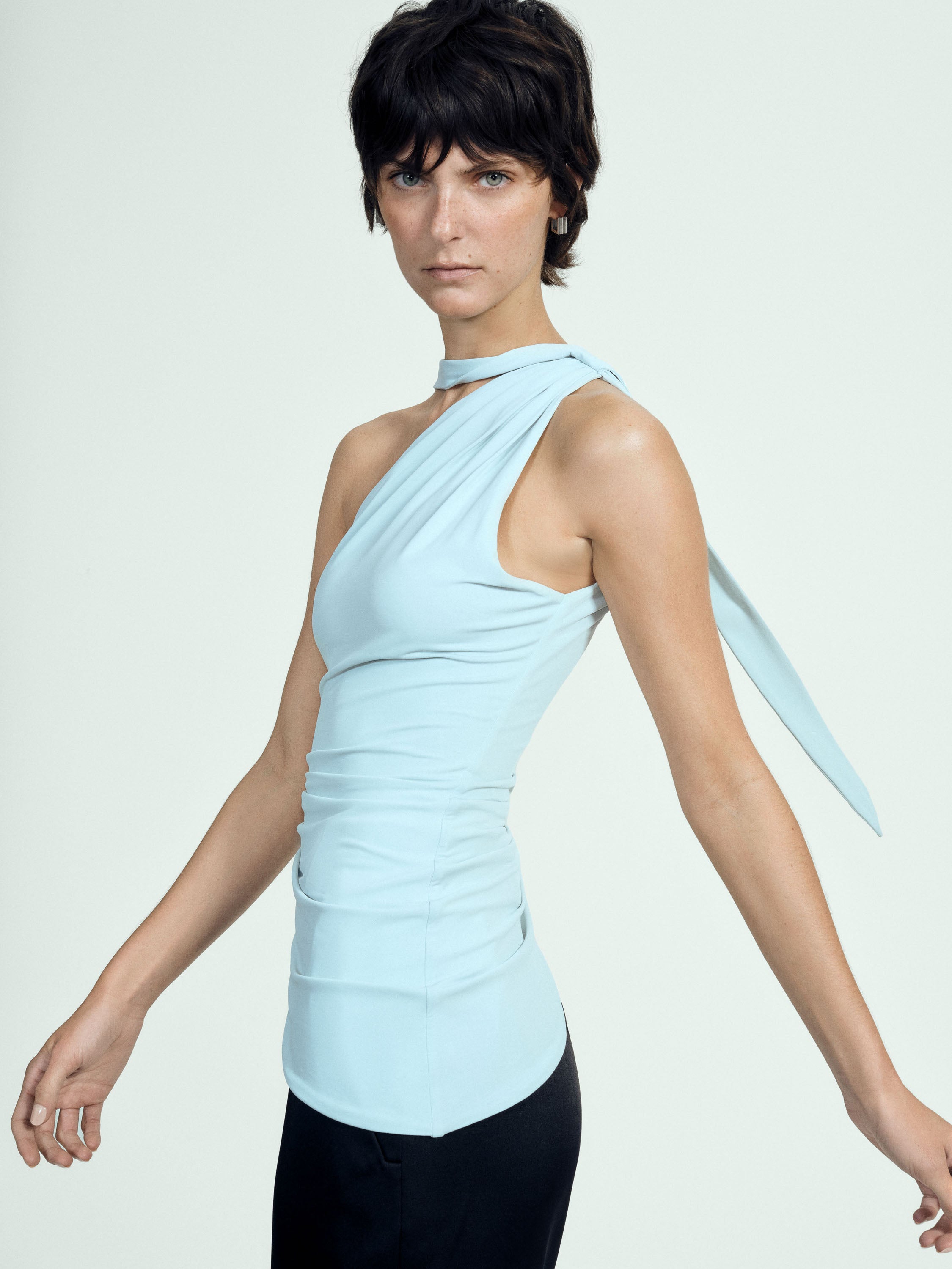 Woman wearing a light blue sleeveless top with a tie detail on a white background