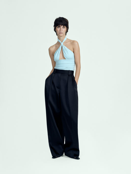 Woman wearing a light blue halter top and black wide-leg pants on a white background