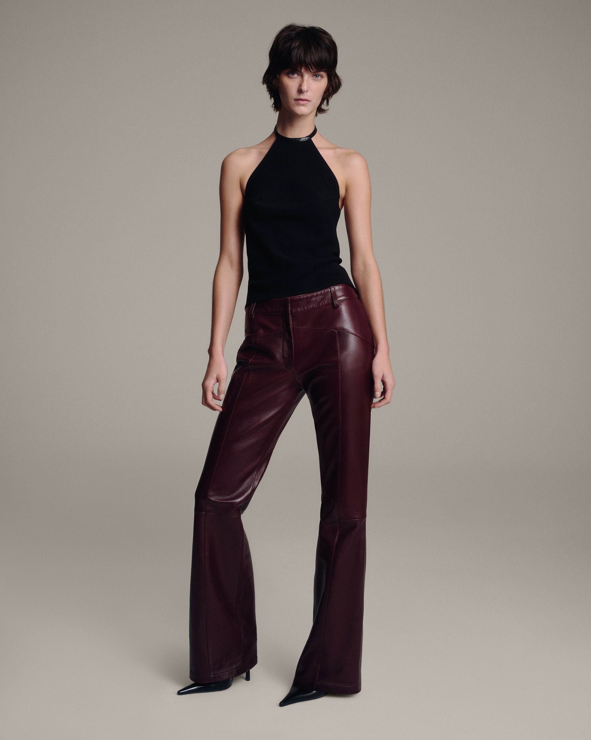 Model wearing a black halter top with burgundy leather flared trousers, full-length front view against a taupe background