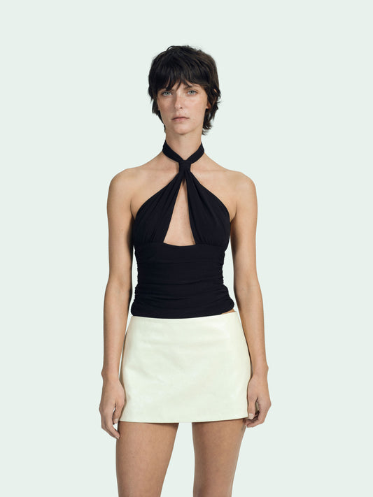 Woman wearing a black halter top and a cream lambskin leather skirt on a white background 