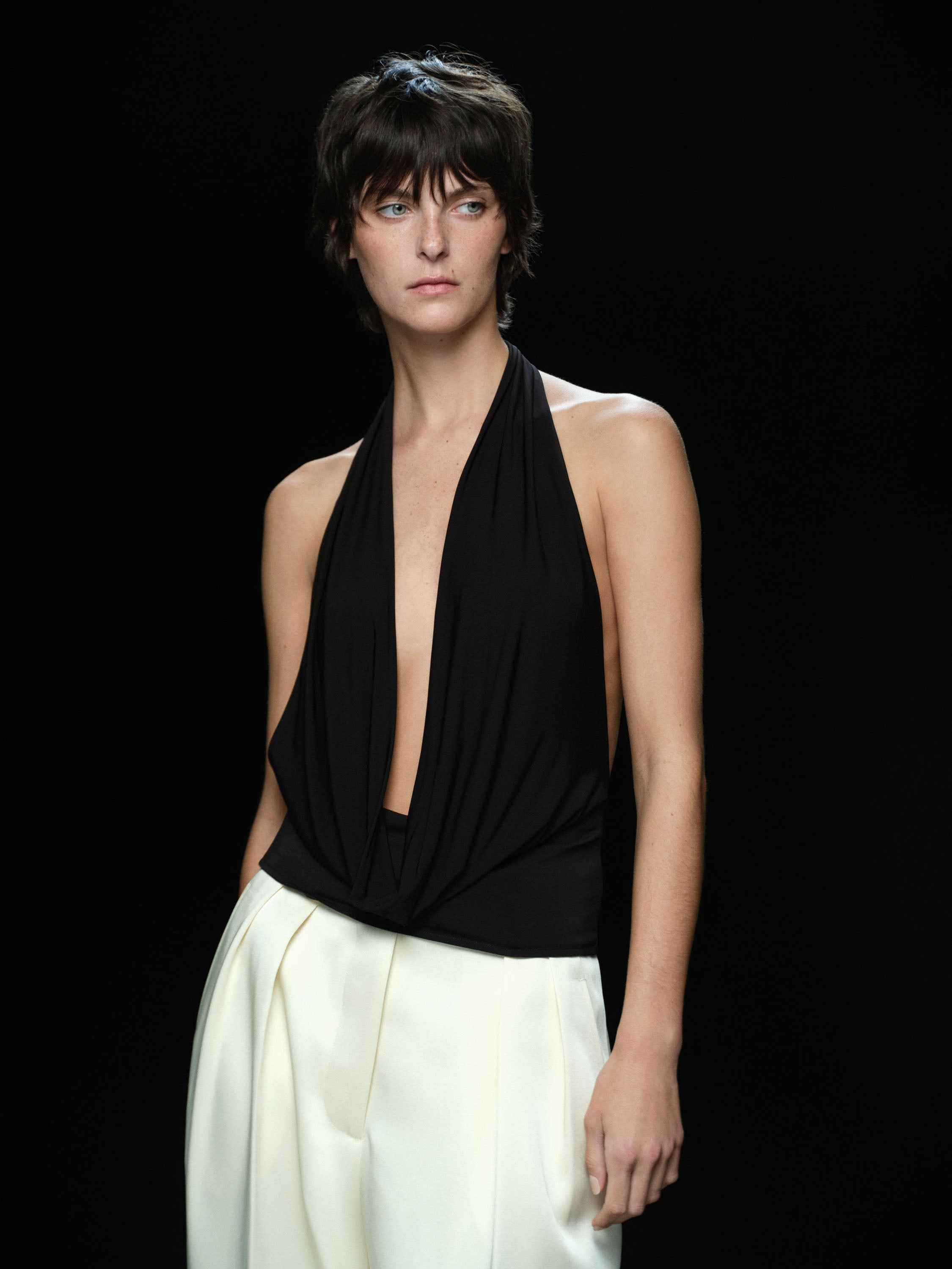 Woman wearing a black halter top and custard satin pants against a black background