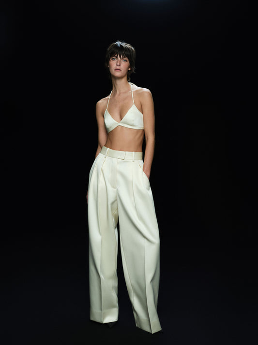 Woman wearing a white satin bra top and wide-leg pants against a black background