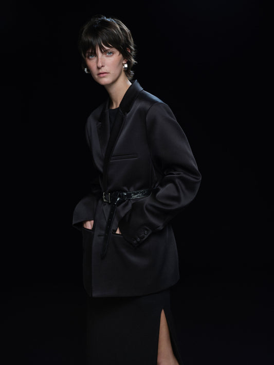 Person wearing a black satin blazer against a black background