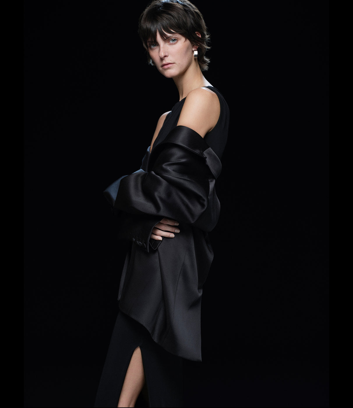 Woman wearing a black dress with a black blazer off the shoulders against a black background