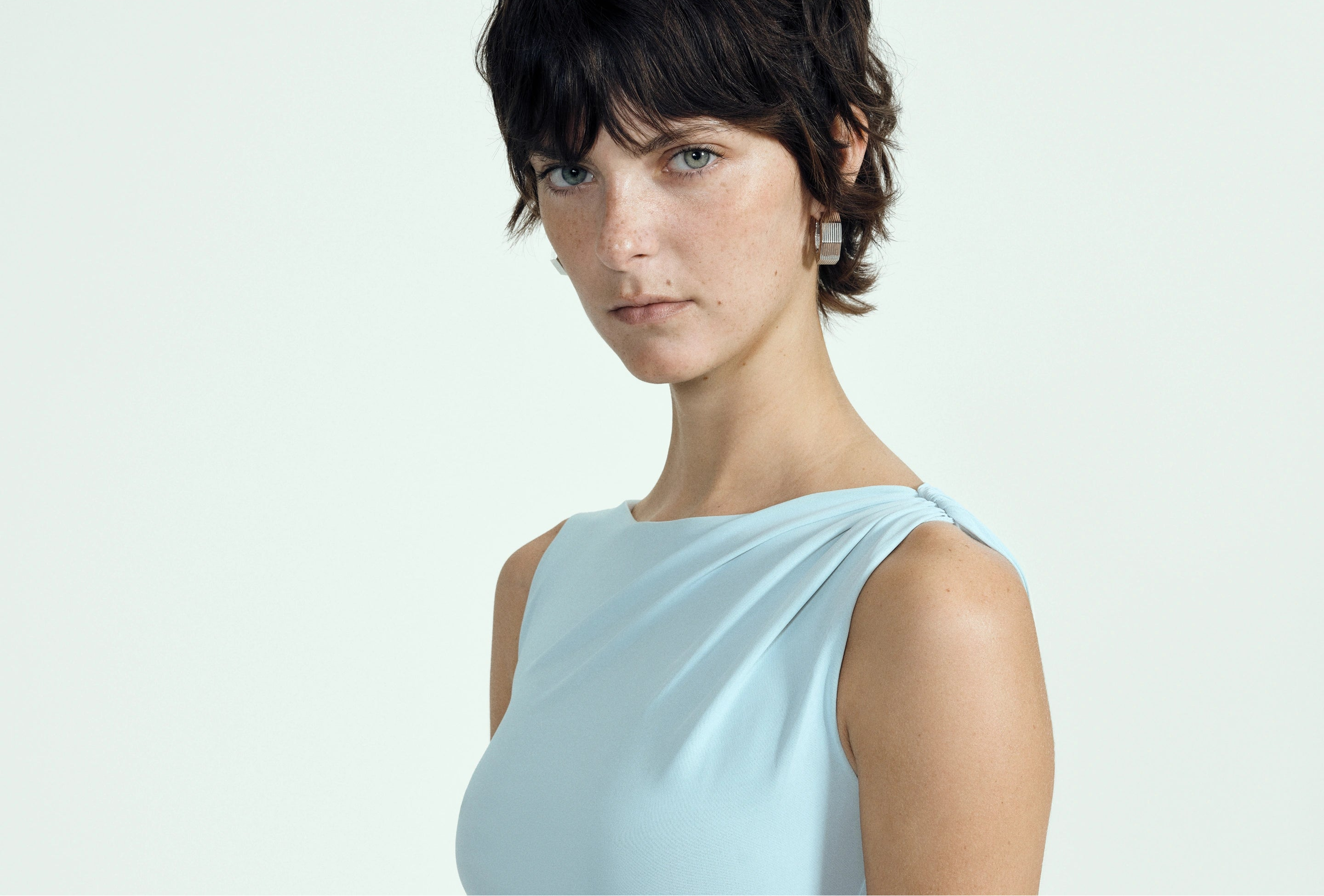 Woman wearing a ice blue sleeveless gown against a plain background