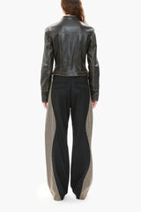 Person wearing a dark brown leather jacket and black pants with patterned hem on a white background