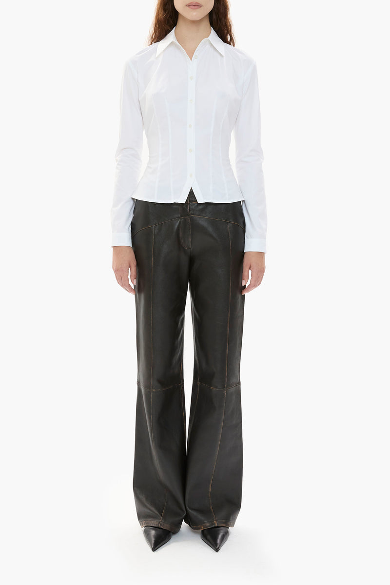Person wearing a white shirt and dark brown leather pants on a white background