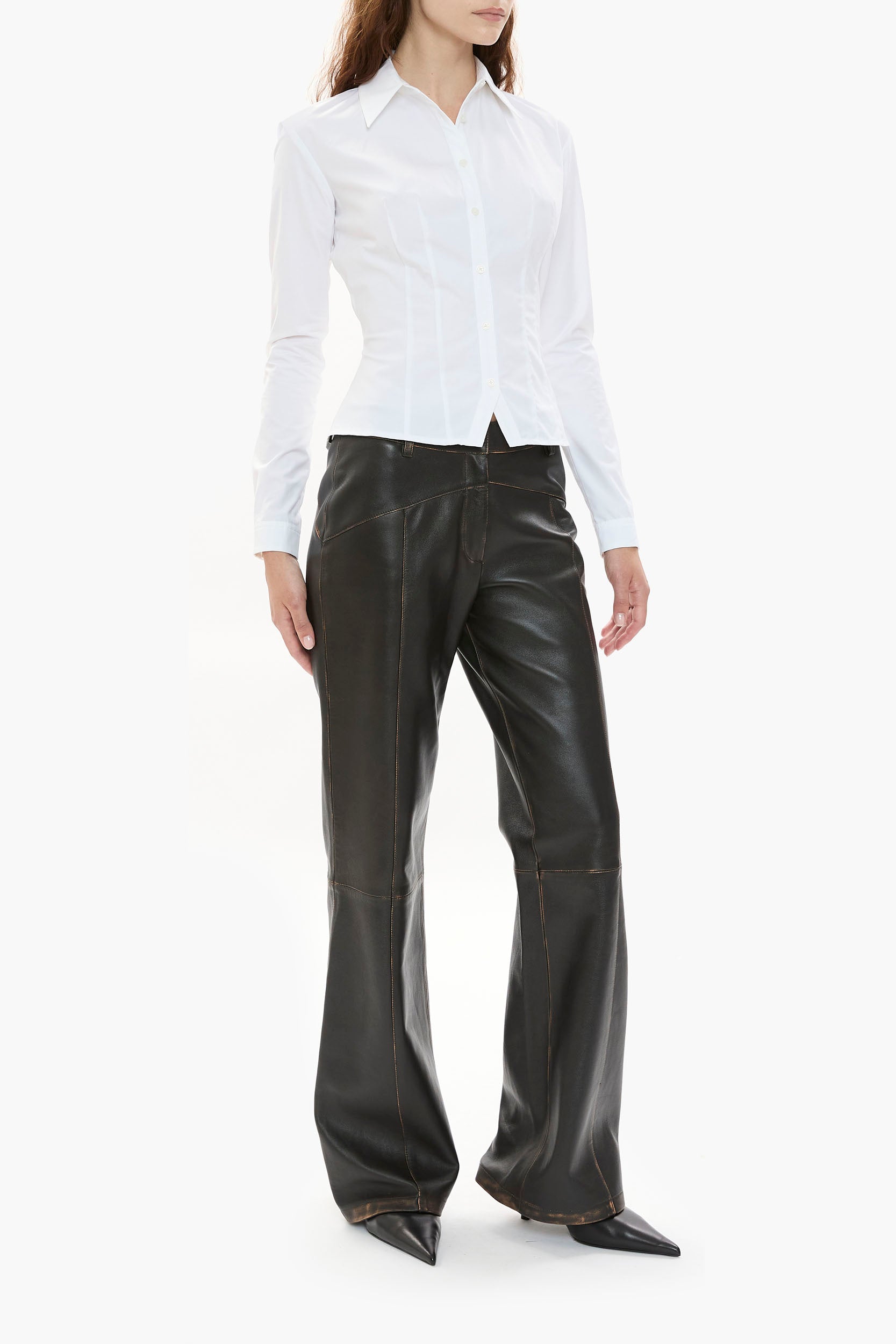 Person wearing a white shirt and dark brown leather pants on a white background