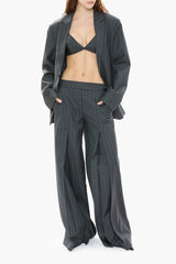 Person wearing a gray pinstripe suit with a bra and high-waisted pants on a white background