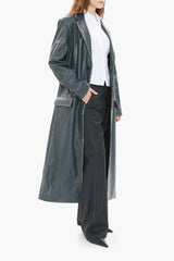 Person wearing a long dark blue leather coat over a white shirt and black pants on a white background